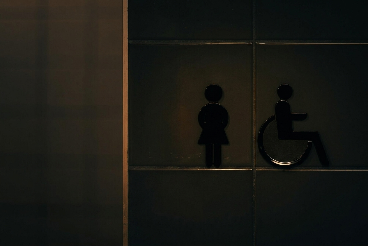 Restroom signage icons on dark near-black tile with warm gold grout highlights